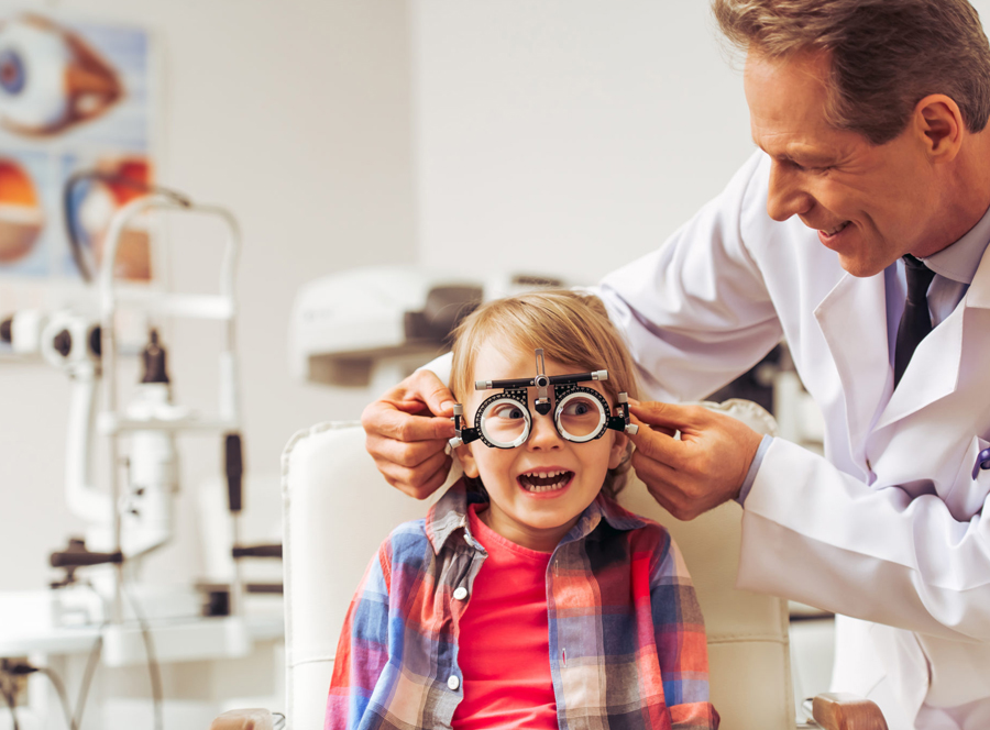 Child undergoing eye exam with optometrist adjusting trial frame.